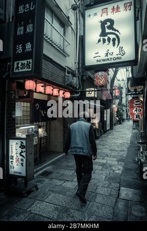 Un uomo che cammina lungo Hozenji Yokocho, un vicolo stretto di bar e ristoranti a Namba, Osaka, Giappone. Foto Stock