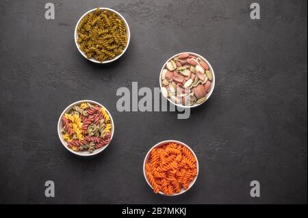 Vari tipi di pasta in ciotole multicolori e sparsi sul classico backgroun rustico scuro. Maccheroni e spaghetti, cucina della pasta italiana Foto Stock