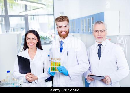 Lavoro di squadra di successo e concetto di team building. Un gruppo di tre assistenti sorride, hanno terminato un esperimento in laboratorio, tutti indossando camici da laboratorio Foto Stock