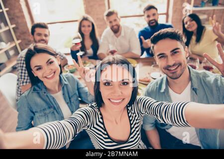 Bella ragazza bruna sta facendo selfie con i suoi amici alla festa sul suo telefono`s fotocamera. Tutti sorridono e godono la loro azienda, divertendosi Foto Stock