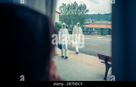 Donna che guarda attraverso la finestra persone in tute di protezione Foto Stock