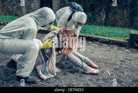 Medici in tute di protezione che si prendono cura di una donna Foto Stock