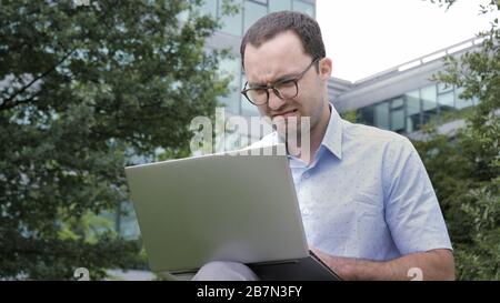 Emozione comica. Giovane uomo d'affari con un'emozione disgustata che tiene il laptop in un parco. Foto Stock