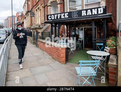 Un uomo che indossa una maschera facciale passa davanti a un caffè a Leeds, West Yorkshire, il giorno dopo che il primo ministro Boris Johnson ha invitato le persone a stare lontano da pub, club e teatri, lavorare da casa se possibile ed evitare tutti i contatti non essenziali e viaggiare per ridurre l'impatto della pandemia di coronavirus. Foto Stock