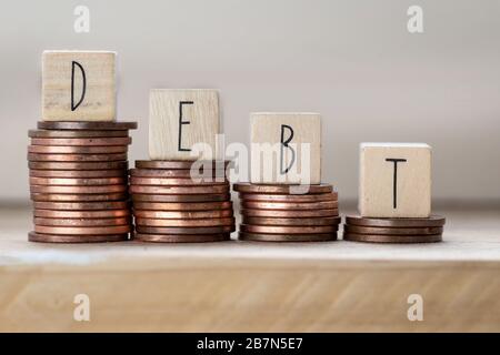 Debito scritto su cubi di legno con lettere, mucchi di denaro di monete, denaro scalando scale sfondo di legno, concetto di business Foto Stock