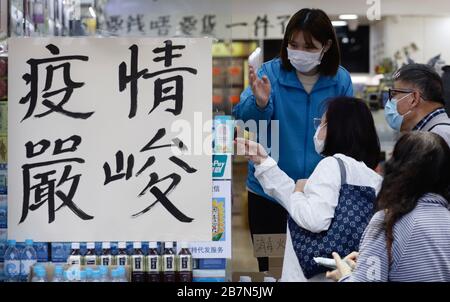 Hong Kong, CINA. 17 Marzo 2020. Assistente di negozio mascherato negoziare con i clienti presso la farmacia locale, poster è esposto al di fuori del negozio che è scritto, LO STATO DELLA PESTE È GRAVE.Mar-17, 2020 Hong Kong.ZUMA/Liau Chung-ren Credit: Liau Chung-ren/ZUMA Wire/Alamy Live News Foto Stock