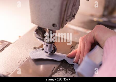 Mani di cucitura, tessuto e macchina da cucire, primo piano. Episodio di lavoro in studio - il processo di personalizzazione, dettaglio primo piano - la macchina, thr Foto Stock