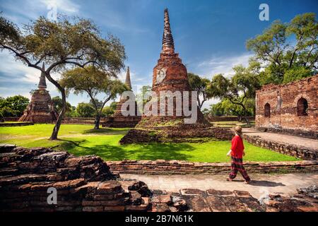 Tourist donna in costume rosso guardando antichi stupa in rovina in Ayutthaya parco storico, Thailandia Foto Stock