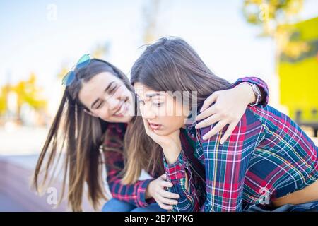 Giovane donna conforta una triste amica femminile nel parco Foto Stock