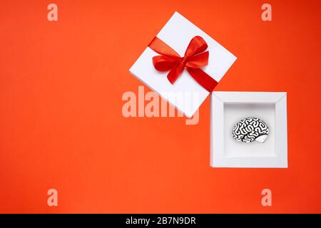 Presente creativo sotto forma di una piccola copia di un cervello umano che giace all'interno di una scatola regalo bianca con un nastro rosso e un arco sulla copertina. Foto Stock