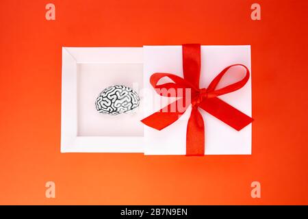 Divertente presente sotto forma di una piccola copia in acciaio di un cervello umano all'interno di una scatola regalo bianca con un nastro rosso e arco sulla copertura. Foto Stock