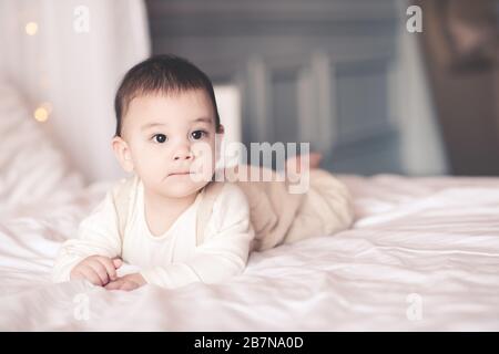 Bambino carino sotto 1 anno di età strisciando in primo piano letto. Guardando lontano. Infanzia. Buongiorno. Foto Stock