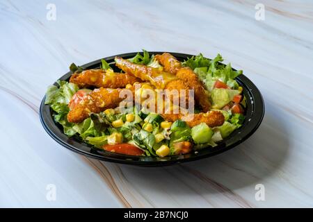 Take away insalata Cajun sana con le dita di pollo e salsa di senape in scatola / confezione di piastra di plastica nera. Fast food biologico. Foto Stock