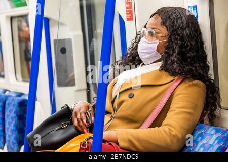 Londra, Regno Unito. 17 Marzo 2020. Una giovane donna nera viaggia verso sud a una distanza di sicurezza dagli altri passeggeri - difese anti Coronavirus (Covid 19), indossando maschere inefectuali sulla Northern Line of London Underground. Credit: Guy Bell/Alamy Live News Foto Stock