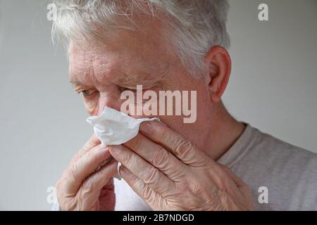 L'uomo più anziano usa un tessuto per soffiare il naso Foto Stock