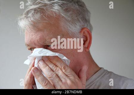 Usando un tessuto, un uomo più anziano soffia il naso con spazio per il testo Foto Stock