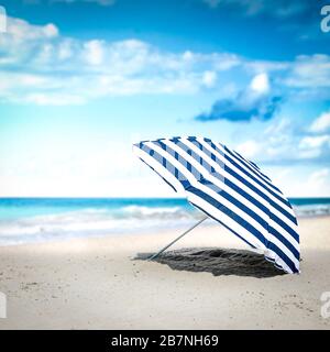 Ombrello blu e bianco sulla spiaggia. Spazio libero per la vostra decorazione. Estate giorno di sole. Cielo blu e paesaggio dell'oceano. Sfondo dell'ora legale. Foto Stock