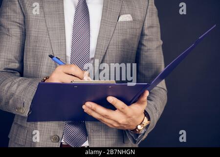 Le mani dell'uomo che scrivono su un foglio di carta in una clipboard Foto Stock