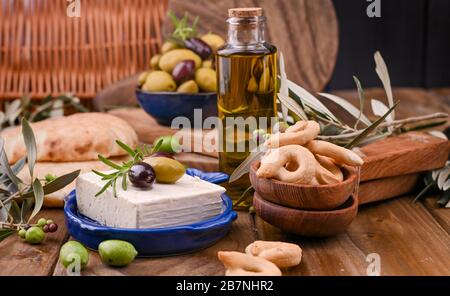 Formaggio greco con olive e CRACKER italiani e ITALIANI o TARALLI . Rami d'oliva freschi, olio d'oliva in bottiglia con spuntini tradizionali italiani. Spazio di copia. Banner Foto Stock
