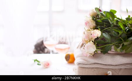 Bouquet di rose luce naturale. Fiori accanto alla finestra e due bicchieri di vino rosato. Atmosfera intima e romantica. Formato lungo banner. Spazio di copia. Messa a fuoco selettiva spostata dal soggetto. Foto Stock