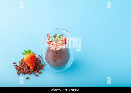 Vegan cioccolato Pudding Chia in vetro decorato con fragola, banana e menta, su sfondo blu, primo piano, spazio copia, posto per testo, orizzontale Foto Stock