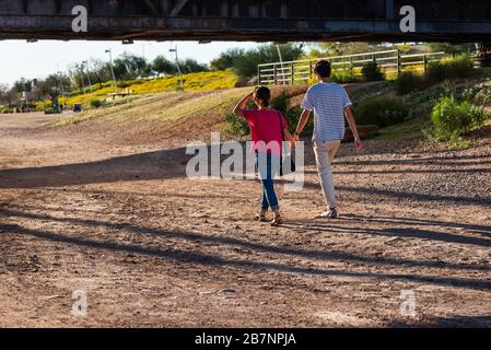 Giovane coppia che cammina e tiene le mani a Tempe North Shore Beach, sotto il Tempe Bridge. Foto Stock