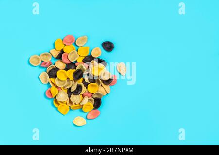 Orecchiette di pasta italiana colorata e cruda su sfondo blu brillante. Vista dall'alto con spazio di copia Foto Stock