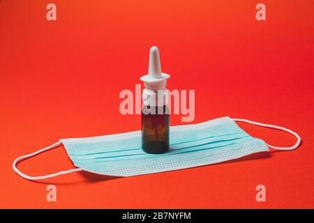 Su sfondo rosso, una bottiglia per naso che cola e allergia, maschera medica. Foto Stock