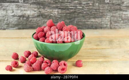 Lampone in una ciotola con bacche sparse intorno su tavolo di legno su sfondo rustico, closeup, spazio copia, sano mangiare vegano e homegro organico Foto Stock