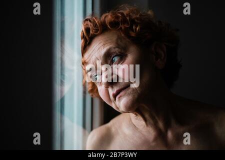 Donna matura per la finestra pensando alla vita Foto Stock