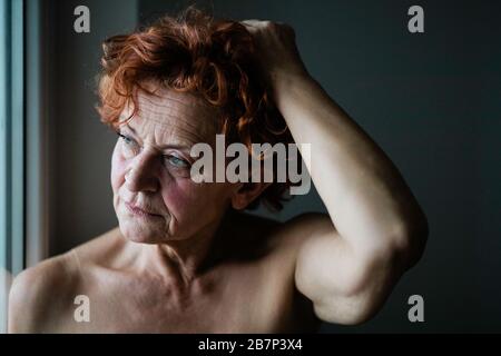 Donna matura per la finestra pensando alla vita Foto Stock