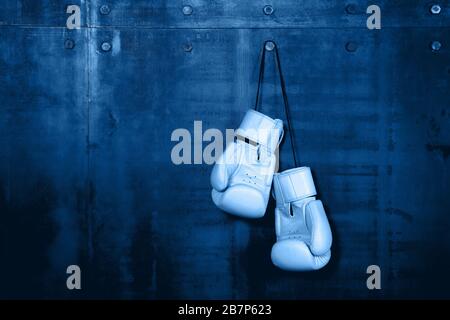Vicino la coppia di classico bianco pelle i guantoni appesi sopra blu scuro muro con spazio di copia Foto Stock