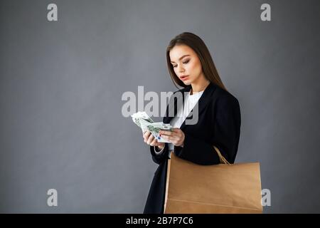 Concetto di shopping. Donna sorridente in possesso di carta shopping bag con spazio copia vuoto per testo e contanti euro, su sfondo grigio Foto Stock