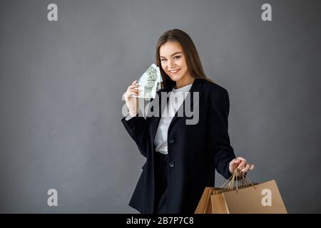 Concetto di shopping. Donna sorridente in possesso di carta shopping bag con spazio copia vuoto per testo e contanti euro, su sfondo grigio Foto Stock