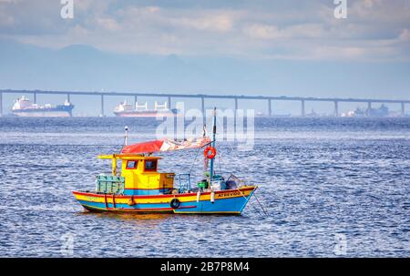 Vista di una piccola barca da pesca colorata ormeggiata nella baia di Guanabara e il ponte Rio-Nitreoi, visto dal quartiere di Urca, Rio de Janeiro, Brasile Foto Stock