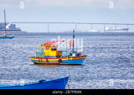 Vista di una piccola barca da pesca colorata ormeggiata nella baia di Guanabara e il ponte Rio-Nitreoi, visto dal quartiere di Urca, Rio de Janeiro, Brasile Foto Stock