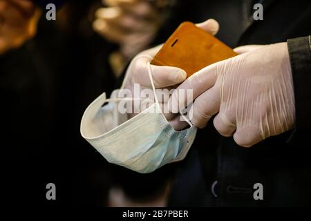 Dettagli con le mani di un uomo in guanti chirurgici che reggono un telefono cellulare e una maschera facciale per evitare la diffusione del COVID-19. Foto Stock