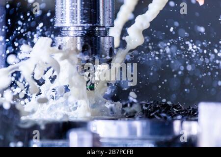 Vista ravvicinata del processo di fresatura verticale in acciaio cnc con flussi di liquido di raffreddamento dell'acqua esterni, schizzi e molti trucioli metallici, contrasto elevato Foto Stock