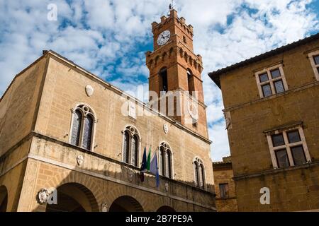 Guardando il Municipio di Pienza in Toscana. Il Campanile ha 2 orologi e si distingue contro i cieli parzialmente blu. Foto Stock