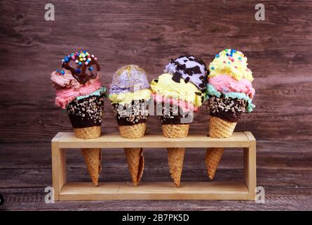 Cono gelato colorato, caramelle arcobaleno, cioccolato e farciture di fragole galleggianti. Gelato estate concetto con condimenti Foto Stock