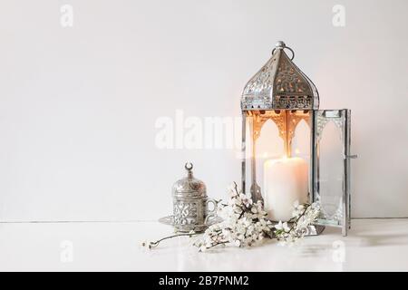 Coppa decorativa d'argento di tè, fiori bianchi, alberi di prunus fiori e lanterna marocchina brillante sullo sfondo del tavolo. Cena IFTAR. Ramadan Kareem saluto Foto Stock
