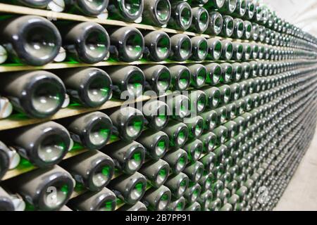 Pile di bottiglie di vino frizzante polverose tappate in un seminterrato scuro. Profondità di campo bassa Foto Stock