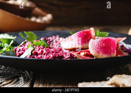 Hummus di rafano di barbabietola con ravanelli di anguria sottaceto su un tavolo di legno rustico, cibo a base di piante, primo piano Foto Stock