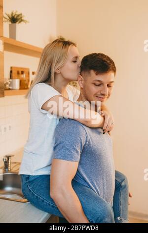 Affascinante signora bionda caucasica abbracciando il suo amante e baciandolo in cucina Foto Stock