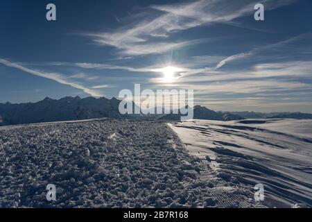 Sera sole con nuvole su altopiano innevato e sullo sfondo di una montagna in Hasliberg. Tracce dal gomaneve nella neve. Foto Stock