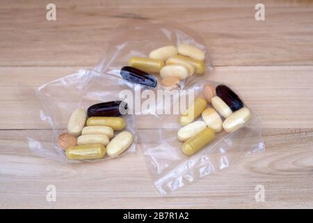 Pillole in confezioni di cellophane su sfondo di legno. Porzioni di tavolette di diverse dimensioni e colori in sacchetti. Supplementi dietetici per effettuare le articolazioni un Foto Stock