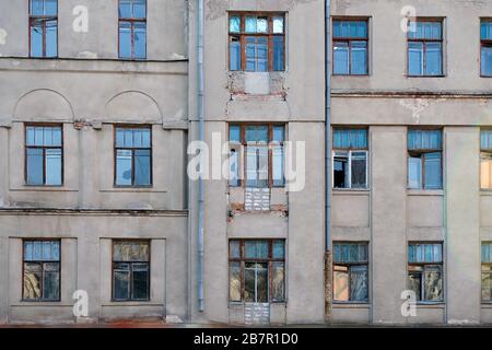 Vecchio edificio facciata con finestre rotte. Edificio grigio a più piani con finestre di dimensioni diverse. Edificio abbandonato con cornici in legno per finestre Foto Stock