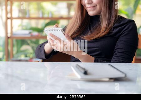 Immagine closeup di una bella donna d'affari che tiene e scrive su notebook in un caffè con sfondo verde natura Foto Stock