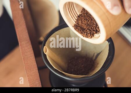 Immagine di primo piano di una mano che versa il caffè dal macinacaffè di legno in un filtro antigoccia Foto Stock