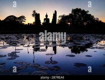 Uno splendido scenario di Wat Mahathat tempio di Sukhothai Historical Park con la statua di Buddha di Silhouette e di riflessioni sullo stagno in Thailandia Foto Stock